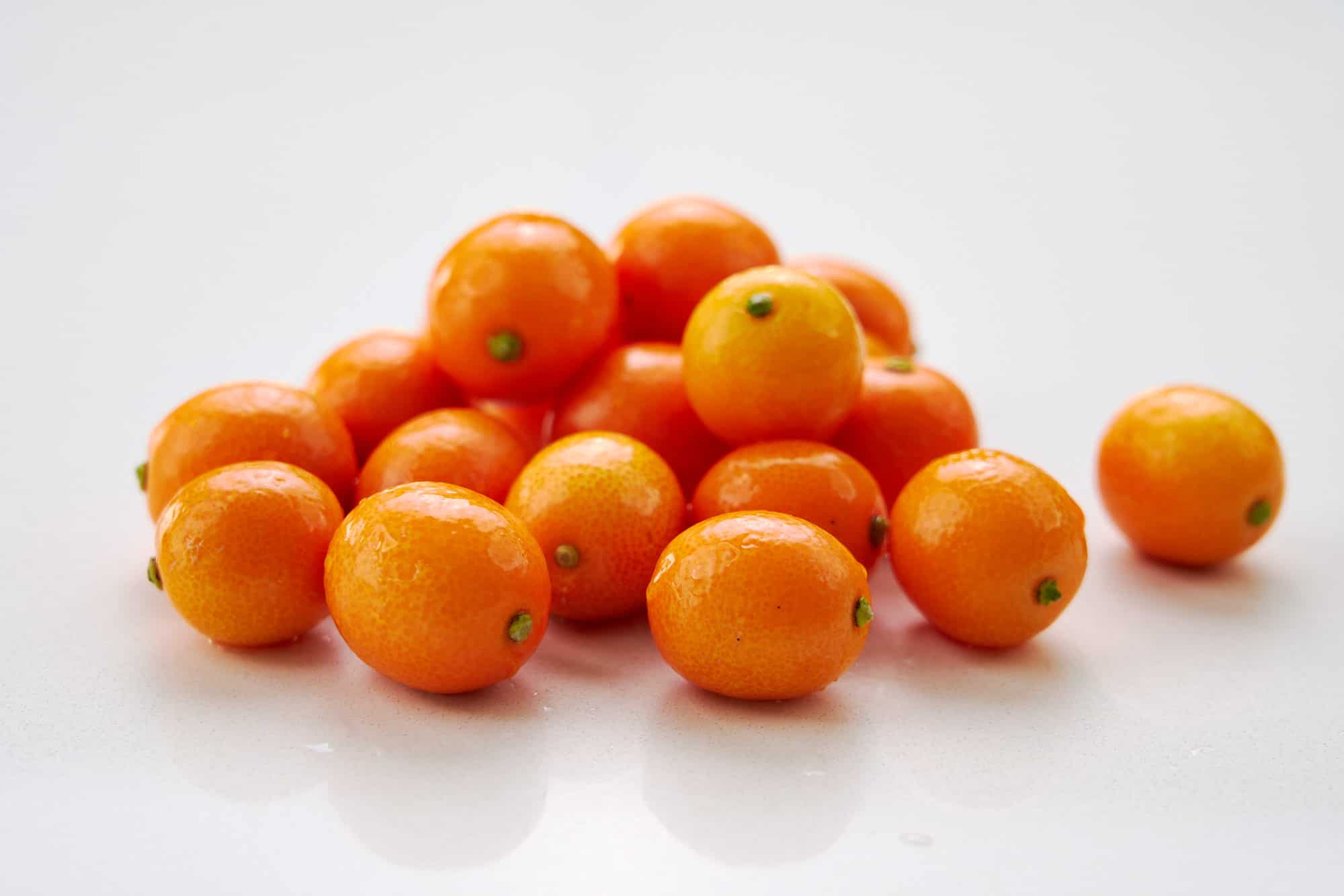 A pile of fresh kumquats on a white surface.