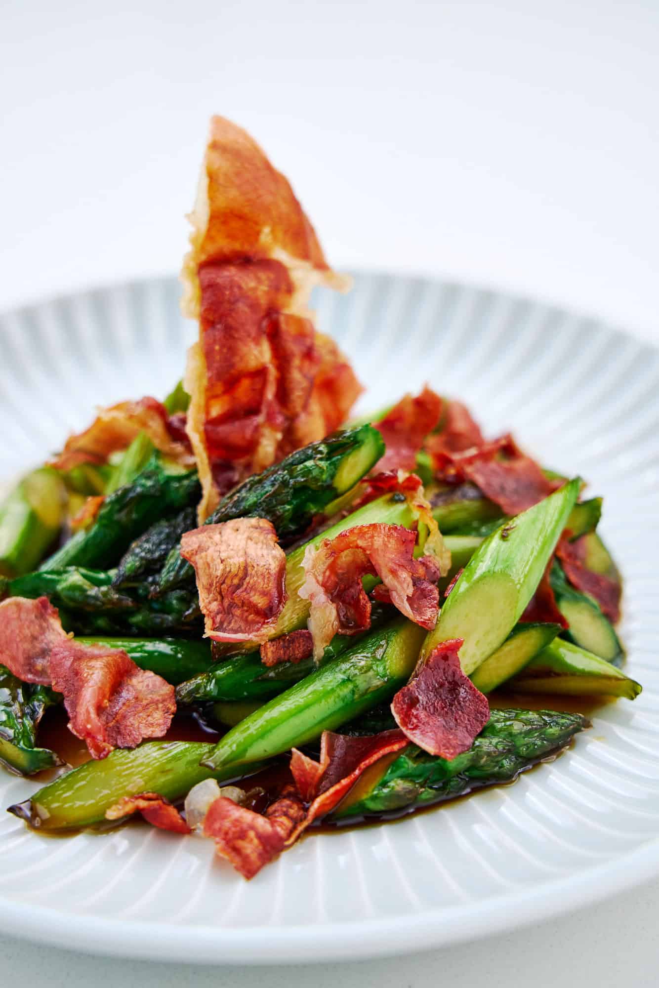 A plate of honey glazed asparagus spears with dry-cured ham that's been crisped in a microwave oven.