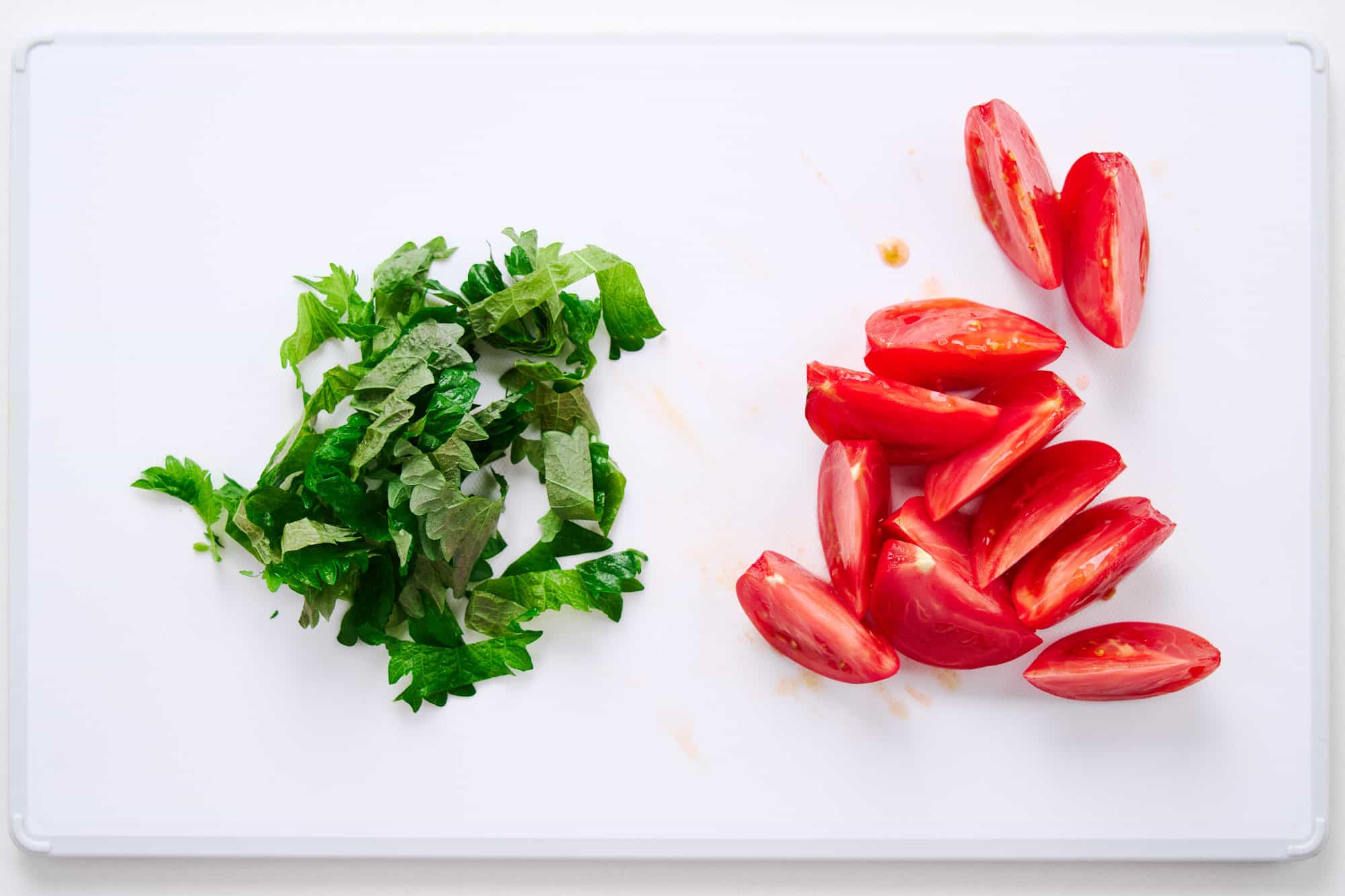 Chopped green shiso leaves with ripe tomato wedges.