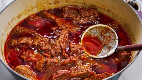 Skimming off excess fat from the braising liquid.