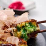 A bite of Negiyaki balanced on chopsticks, ready to eat.