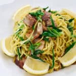 A plate of stir fried noodles with pork and scallions.