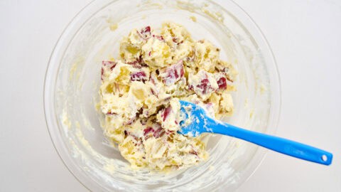 Mixing in the dressing and mashing the potatoes.