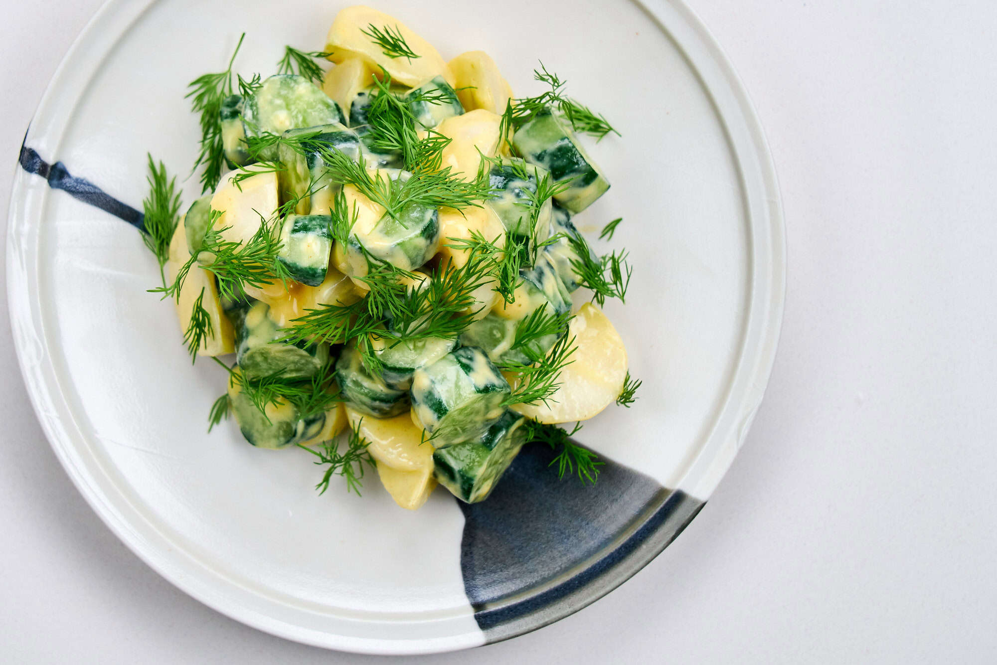 Cucumber Dill Salad with Dijon Mustard plated on white. Salted cucumbers and turnips piled high and topped with fresh dill fronds.