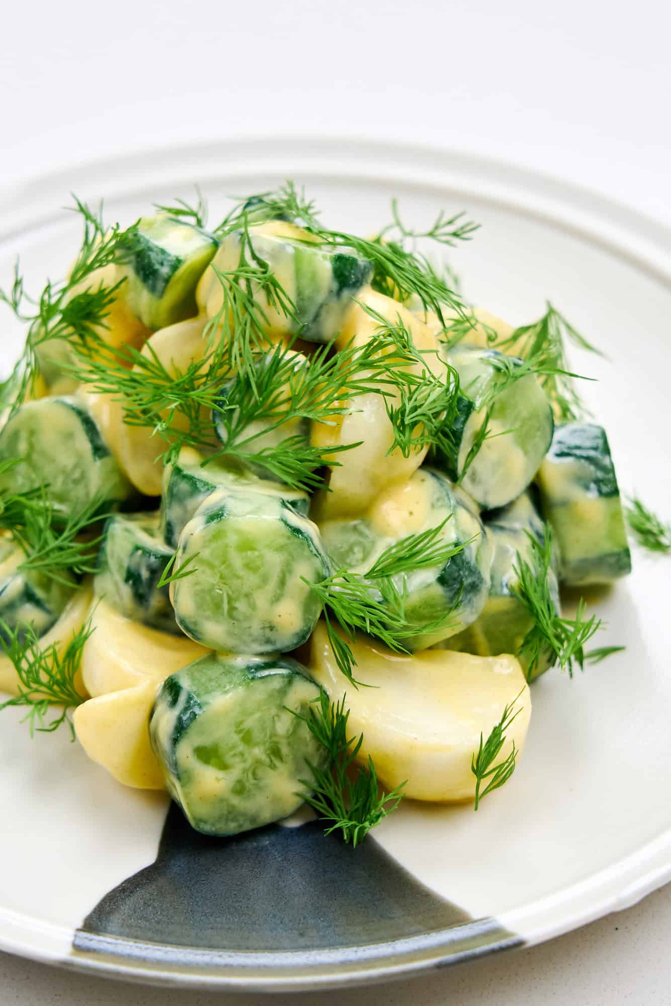 Cucumber Dill Salad with Dijon Mustard stacked tall on a plate, salted cucumbers and turnips coated in mustard and showered with dill.