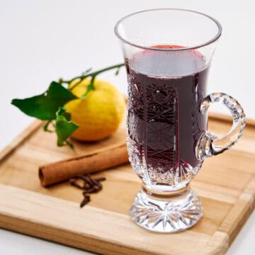 Mug of Japanese gl&uuml;hwein on a wooden serving board with fresh yuzu, a cinnamon stick, and cloves arranged beside it.