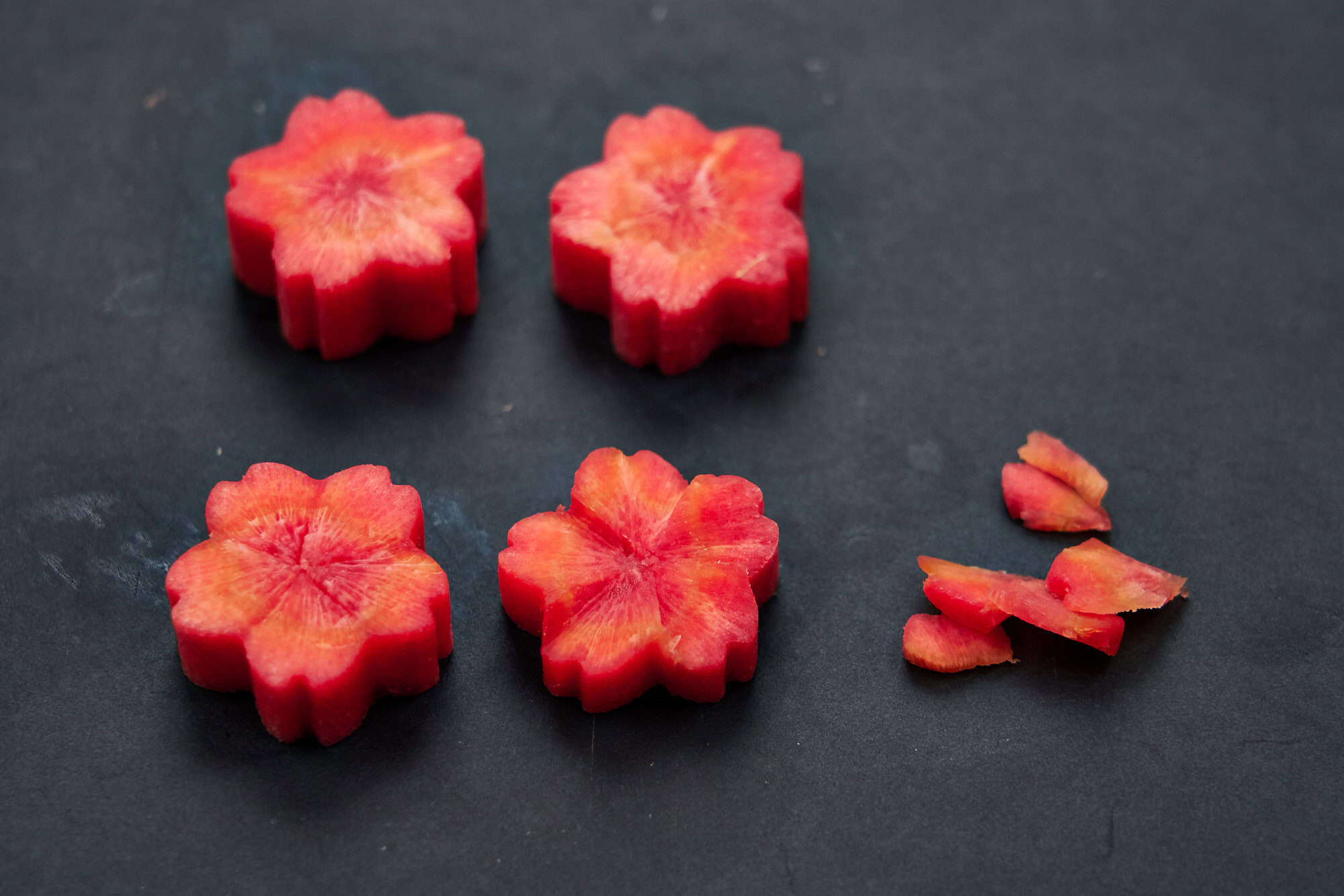 Scarlet kintoki carrot rounds carved into cherry blossom flowers, a festive New Year garnish for Tokyo-style ozoni.