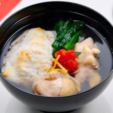Tokyo-style ozoni in a lacquer bowl with toasted kirimochi, tender chicken, spinach, carrot flower, and yuzu garnish.