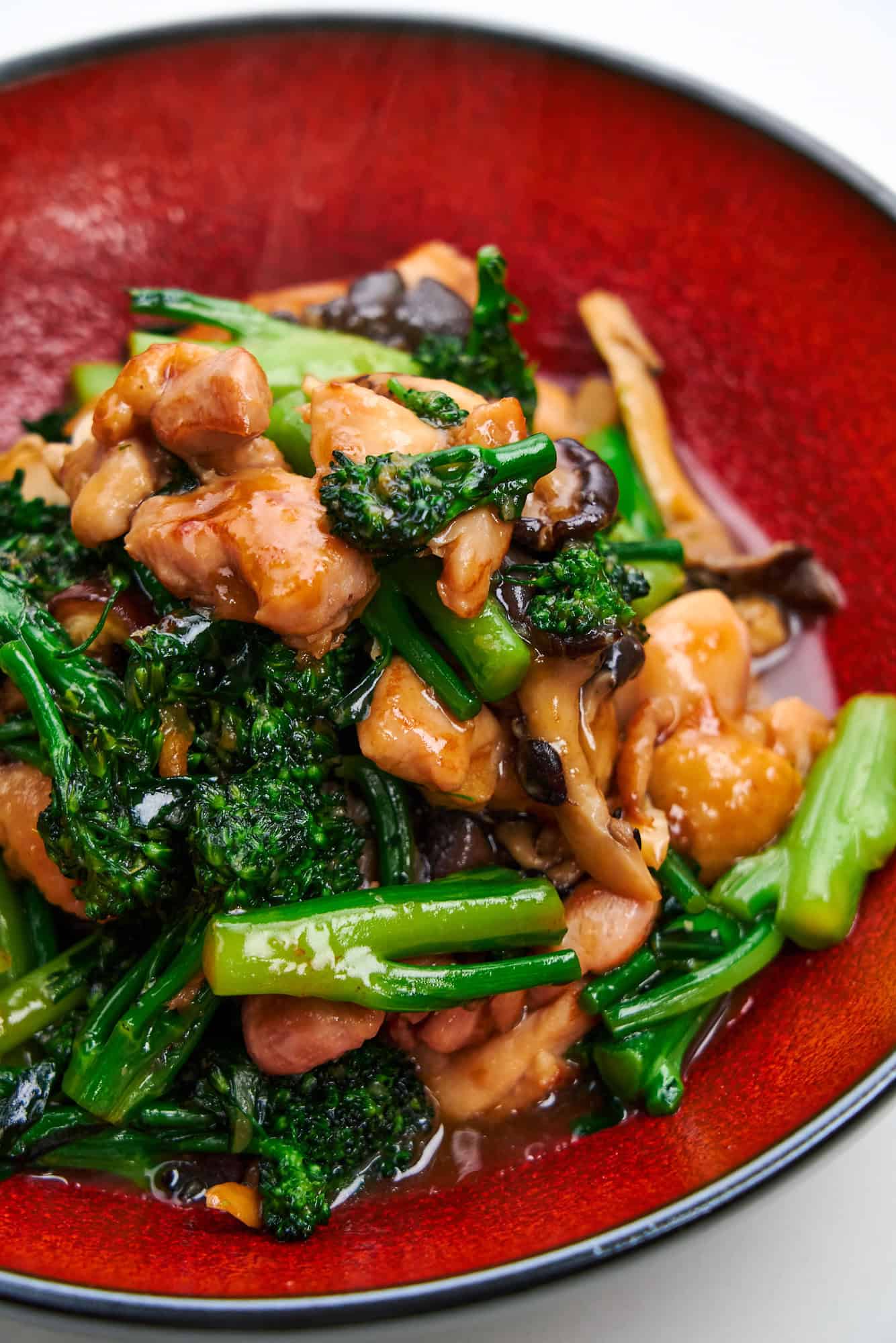 A red plate holds verdant broccolini and tender chicken.