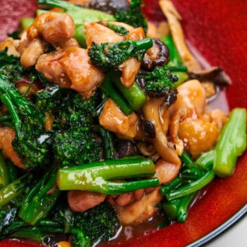 A red plate holds verdant broccolini and tender chicken.