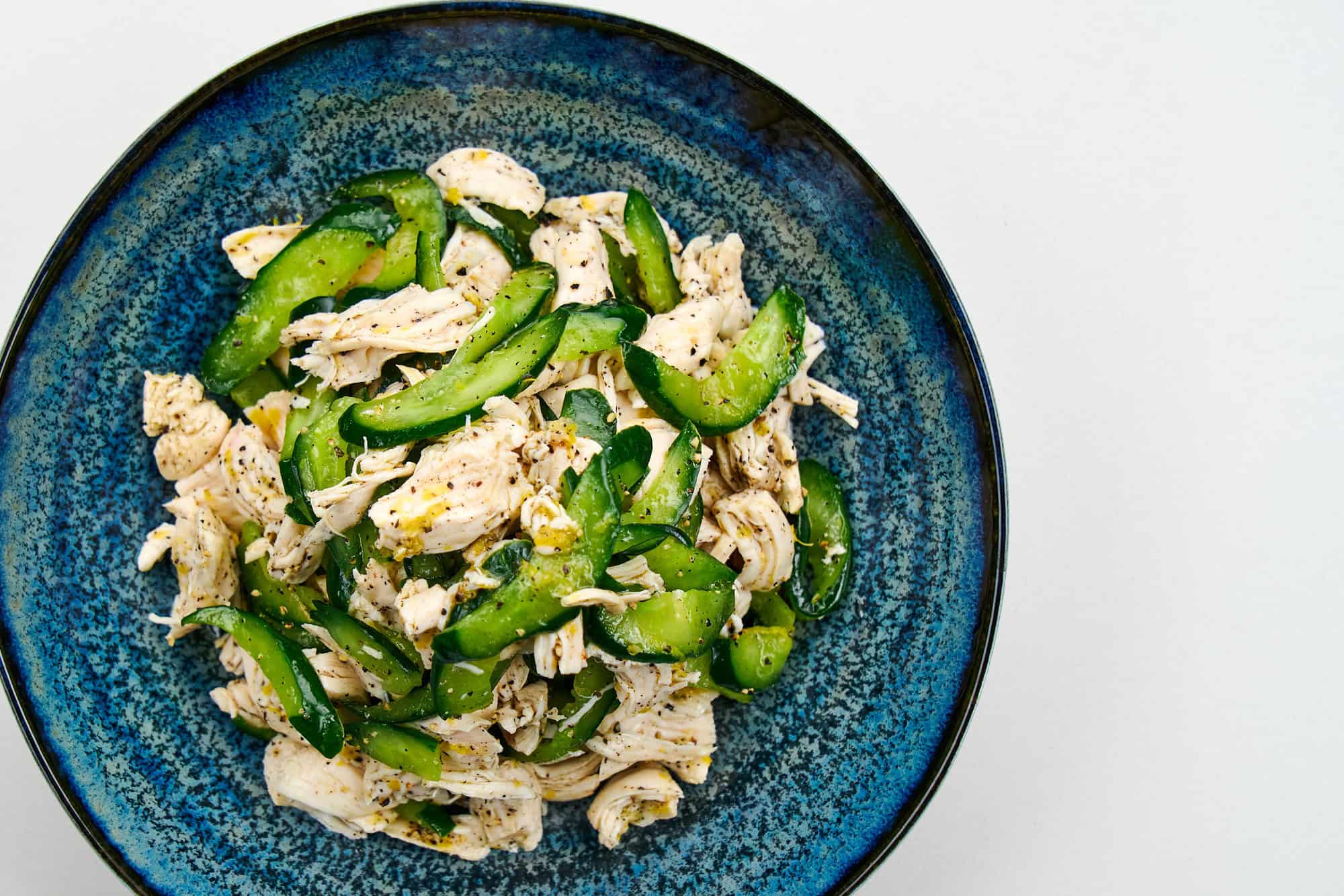Finished lemon pepper chicken salad plated in a vibrant blue bowl, scattered with crunchy cucumbers and peppery chicken.