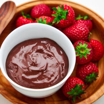 A bowl of chocolate pudding surrounded by strawberries.