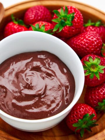A bowl of chocolate pudding surrounded by strawberries.