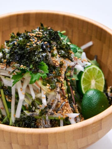 A wooden bowl of greens and citrus with daikon.