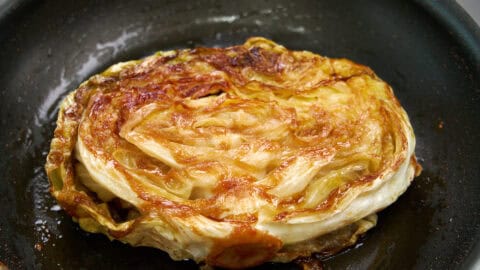 Deeply caramelized cabbage "steak" in a frying pan.