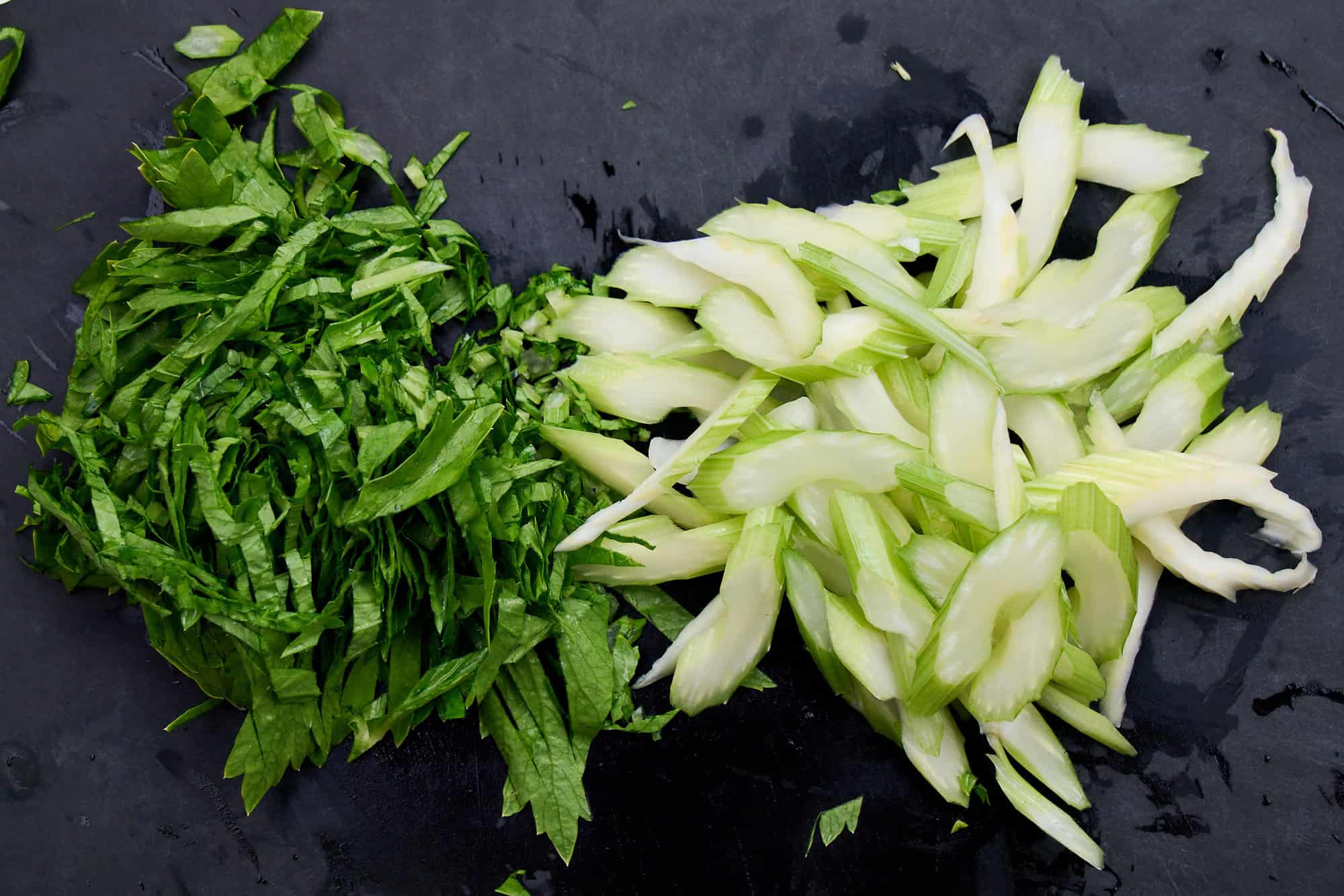 Sliced celery and celery leaves on a black cutting board.