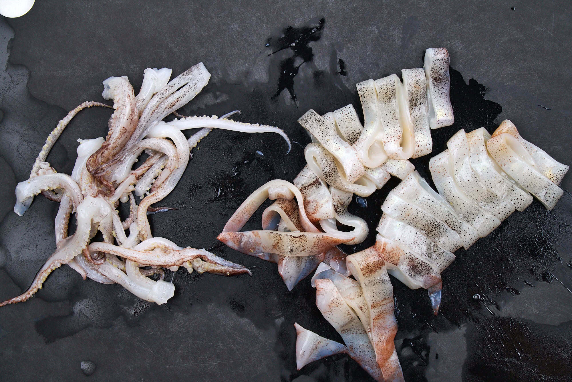 Slices of squid on a black cutting board.