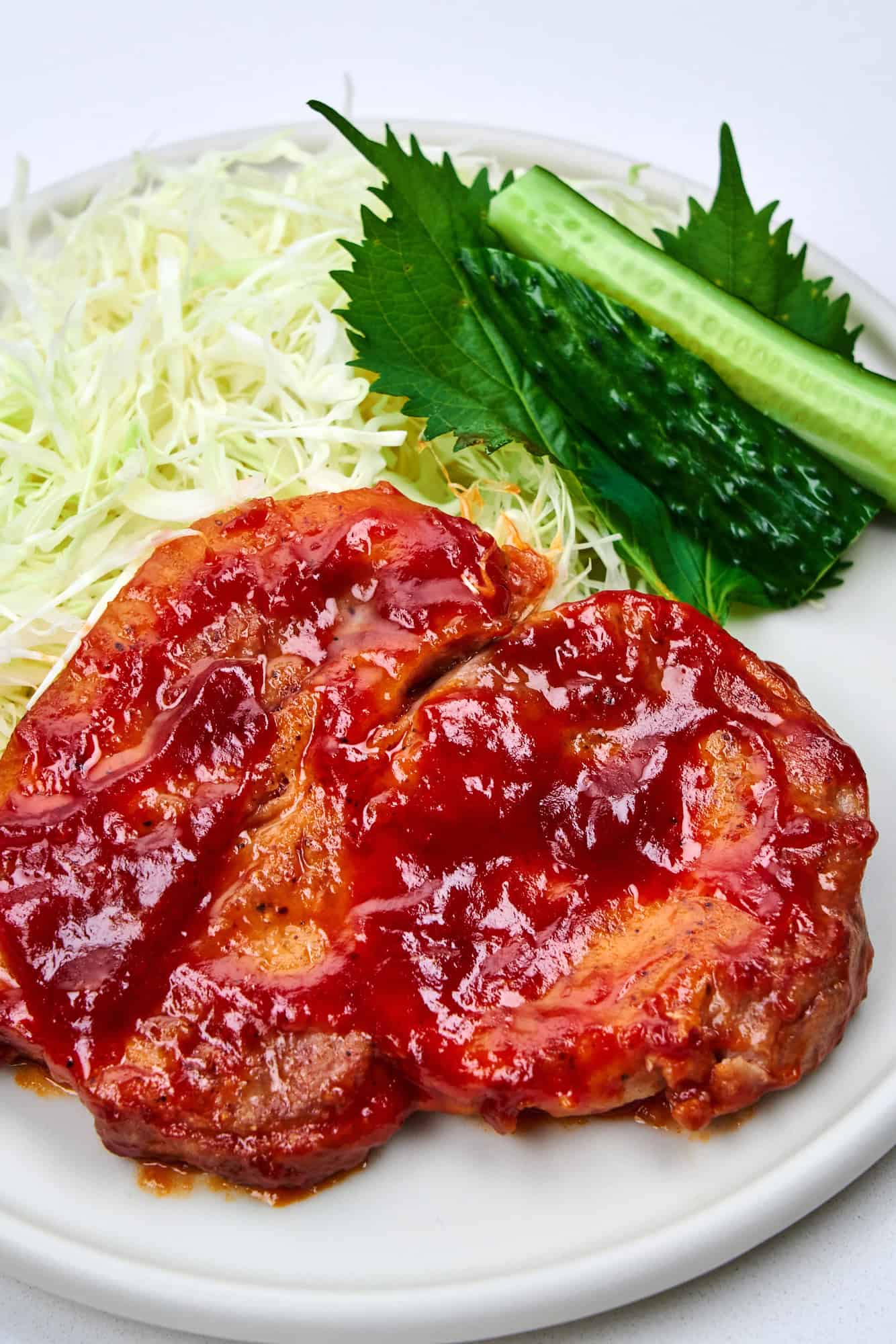 Tangy glazed pork chops on a plate with shredded cabbage and shiso.