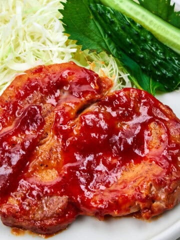 Tangy glazed pork chops on a plate with shredded cabbage and shiso.