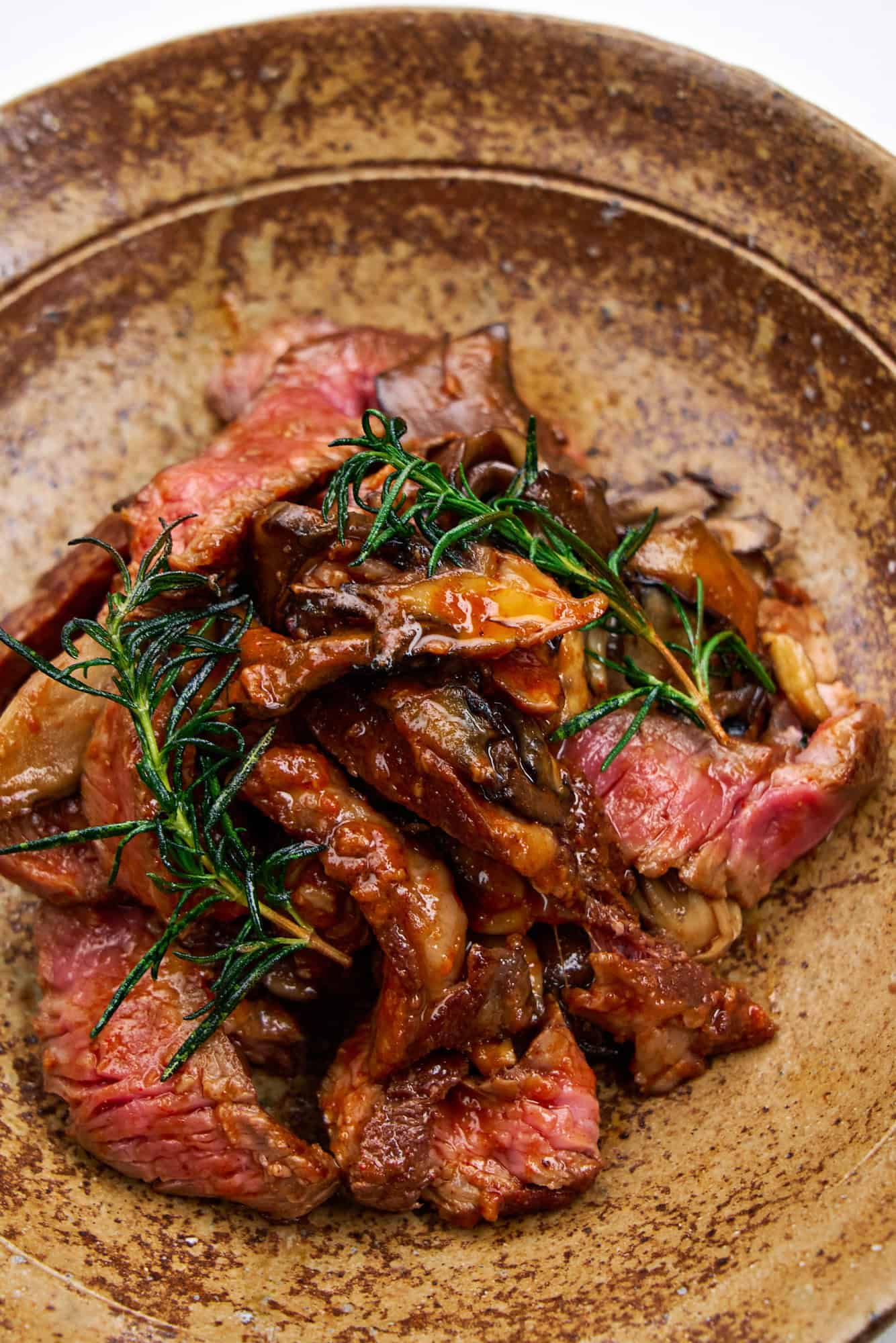 Close-up of pan-fried ribeye with maitake, rosemary, and bravas sauce on a ceramic plate