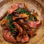 Close-up of pan-fried ribeye with maitake, rosemary, and bravas sauce on a ceramic plate