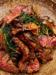Close-up of pan-fried ribeye with maitake, rosemary, and bravas sauce on a ceramic plate