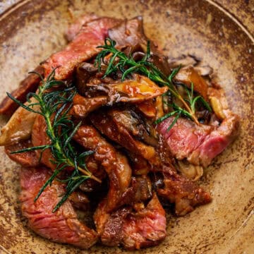 Close-up of pan-fried ribeye with maitake, rosemary, and bravas sauce on a ceramic plate