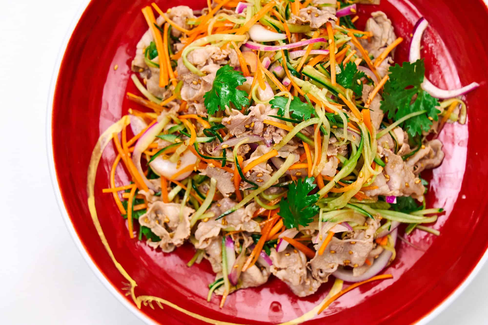 Pork shabu shabu salad with ginger soy dressing, topped with cilantro on a red plate